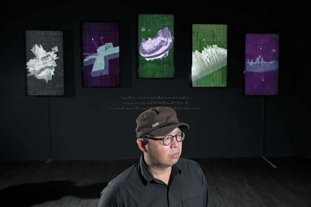 Aluan Wang standing before an audiovisual installation